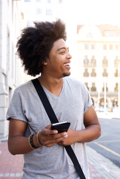 Feliz joven caminando en la ciudad con teléfono móvil