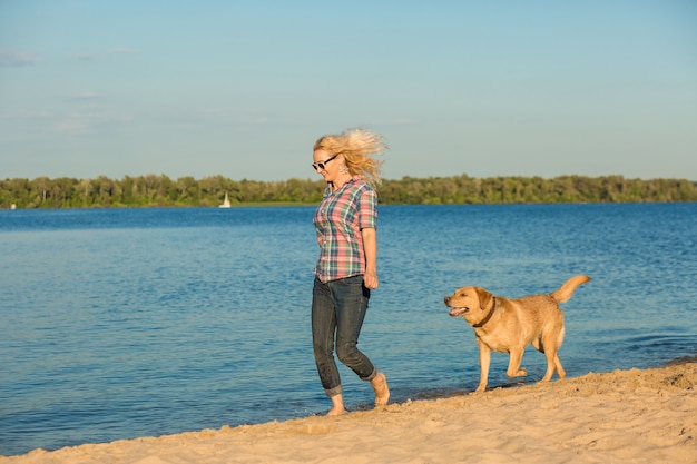 Feliz joven caminando por la playa con su golden retriever al atardecer