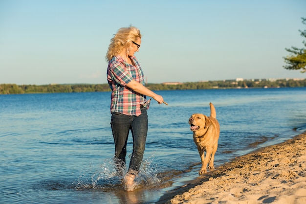 Feliz joven caminando por la playa con su golden retriever al atardecer