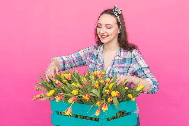 Feliz joven caucásica con caja de tulipanes amarillos sobre fondo rosa