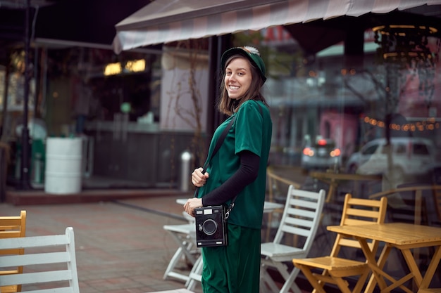 Feliz joven caucásica en vestido verde está caminando cerca de la acogedora cafetería