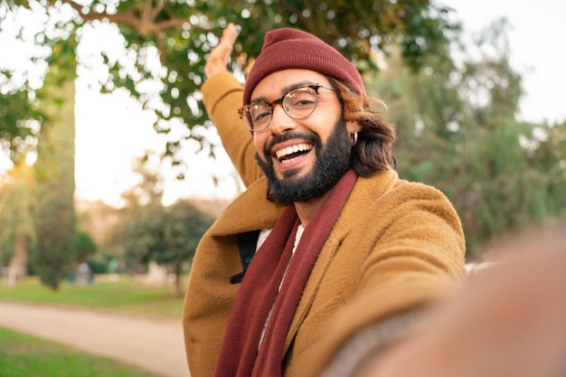 Feliz joven caucásico con gafas y barba tomando un selfie al aire libre en el parque en invierno