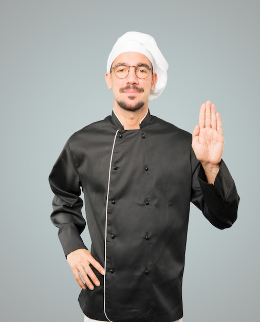 Feliz joven chef haciendo un gesto de parada con la palma de su mano