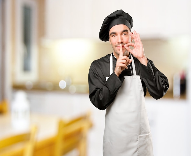 Feliz joven chef haciendo un gesto de silencio