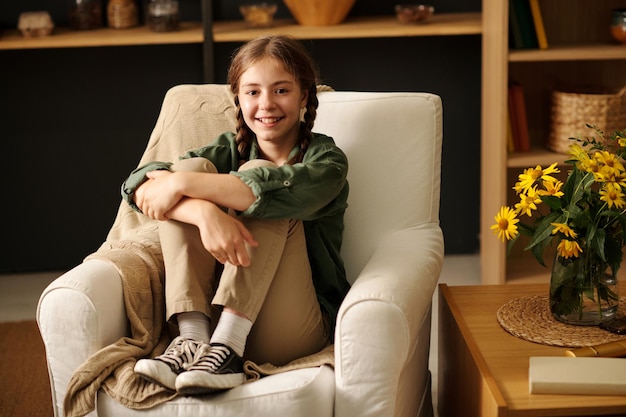 Feliz joven con coletas sentada en un cómodo sillón blanco