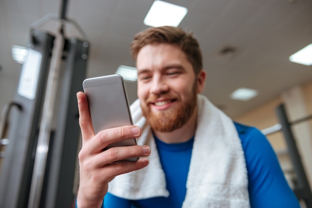 Feliz joven deportista en el gimnasio mirando el teléfono.