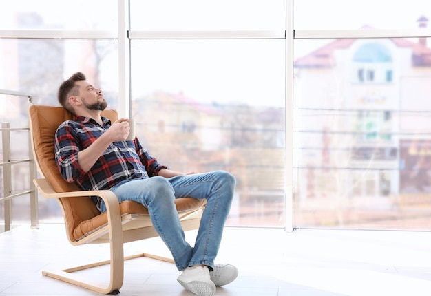 Feliz joven descansando en un sillón con una taza de café