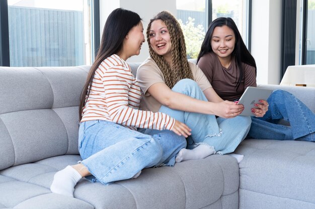 Feliz joven despreocupada diversidad mujeres amigas en casual usando tableta divirtiéndose juntos en casa