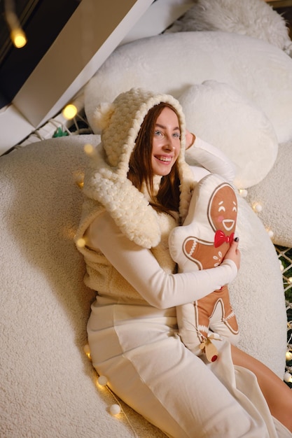 Feliz joven divertida mujer con sombrero de suéter blanco cálido posando sostener galleta de jengibre hombre almohada retrato de estudio Feliz celebración de Año Nuevo concepto de vacaciones