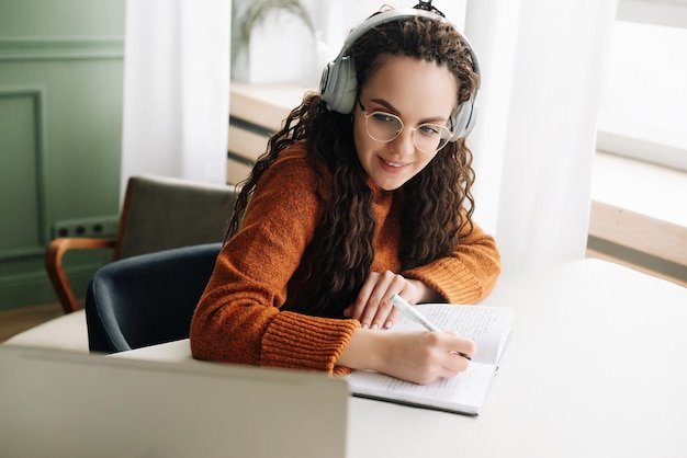 Feliz joven elearning en una computadora portátil desde casa asistiendo a un seminario web con auriculares Estudiante sonriente viendo una clase virtual o teniendo una reunión de conferencia web en la computadora