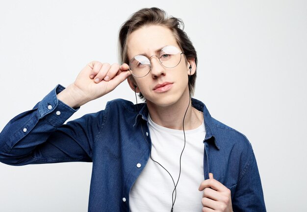 Feliz joven elegante con ropa informal y anteojos ajustando sus auriculares y sonriendo