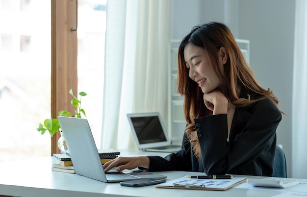 Feliz joven empresaria asiática sentada en su lugar de trabajo en la oficina