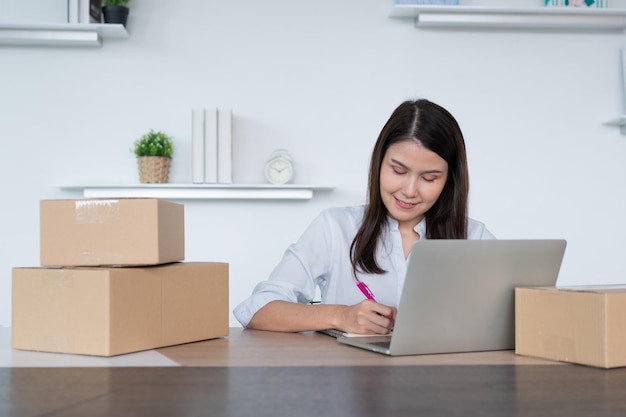 Feliz joven empresaria asiática Tome nota después del pedido de cheques y Sonría para el éxito de la venta