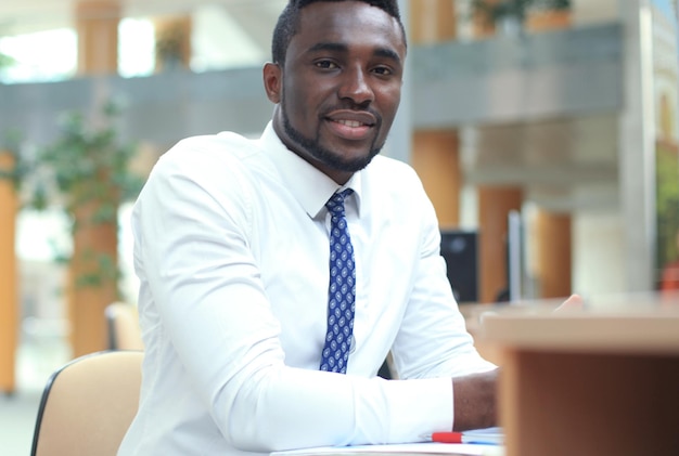 Feliz joven empresario afroamericano mirando la cámara en el lugar de trabajo en la oficina.