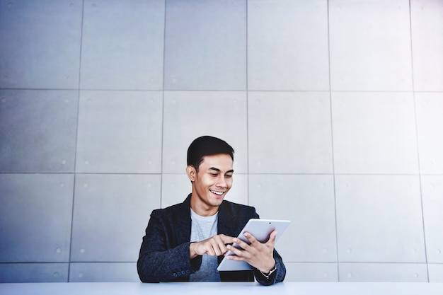 Feliz joven empresario asiático trabajando en tableta digital. Sonriendo y sentado