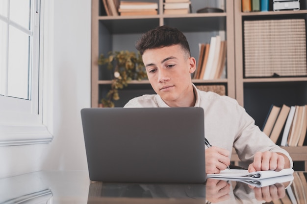 Feliz joven empresario caucásico sonriendo trabajando en línea viendo podcast de seminarios web en la computadora portátil y el aprendizaje de conferencias telefónicas de cursos de educación hacer notas sentarse en el escritorio de trabajo, concepto de elearning