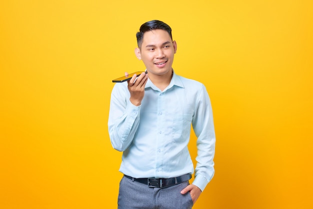 Feliz joven empresario guapo hablando por un teléfono inteligente sobre fondo amarillo