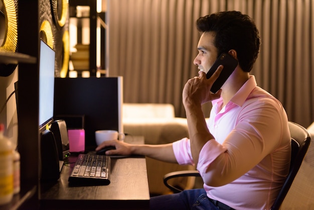 Feliz joven empresario indio hablando por teléfono mientras trabaja horas extras en casa
