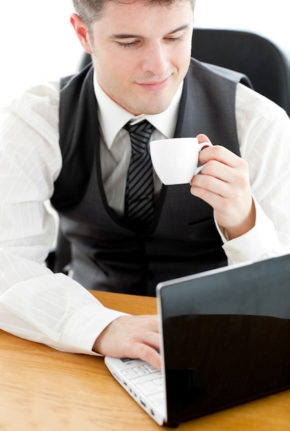 Feliz joven empresario mirando su portátil con un café