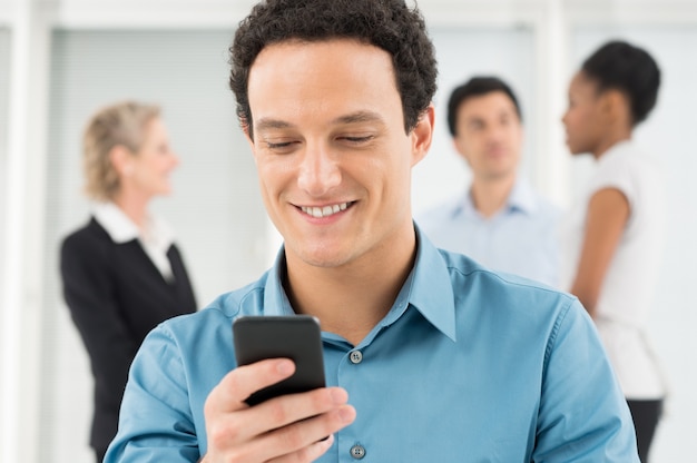 Feliz joven empresario mirando el teléfono móvil en la oficina