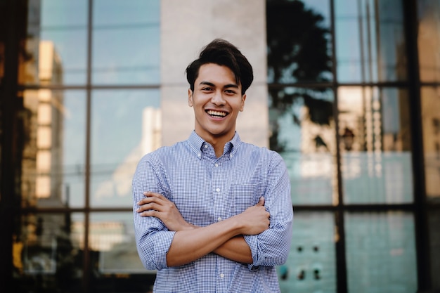 Feliz joven empresario de pie con una gran sonrisa en la ciudad. Brazos cruzados