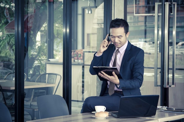 Feliz joven empresario sentado en la cafetería, hablando por móvil