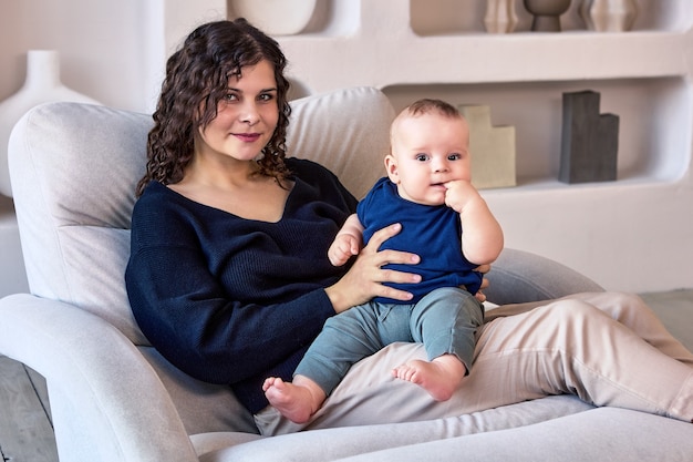 Feliz joven está sentada en el sofá con el bebé