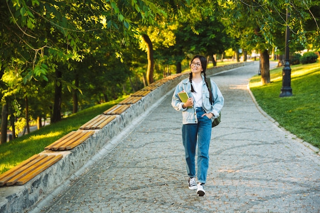 Feliz joven estudiante adolescente llevando mochila y libros mientras camina al aire libre en el parque
