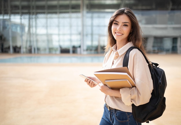 Feliz joven estudiante europea en casual con libros de mochila y teléfono inteligente para ir a estudiar