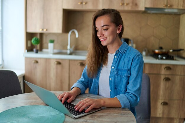 Feliz joven exitoso freelancer milenario inteligente que trabaja en línea en la computadora portátil de forma remota en casa. Usar la computadora para escribir, chatear, navegar y las redes sociales