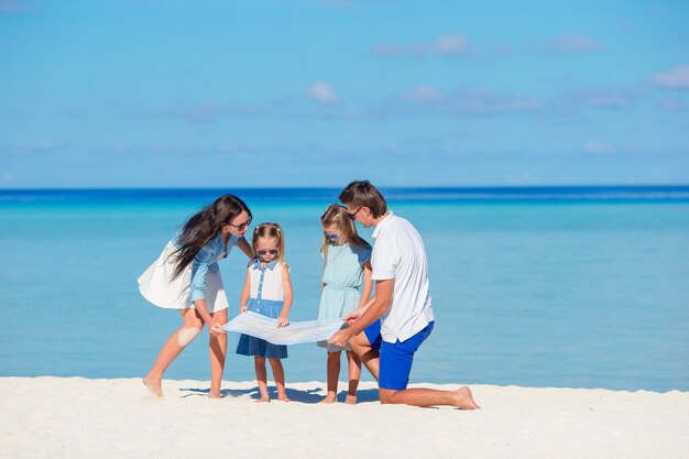 Feliz joven familia de cuatro con mapa en la playa