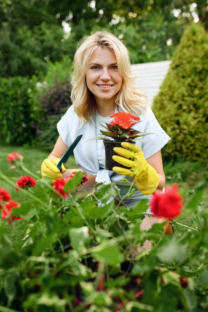 Feliz joven en guantes trabaja con flores en el jardín