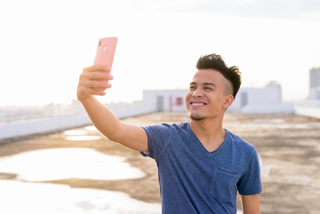 Foto feliz joven guapo multiétnico tomando selfie en la azotea del edificio