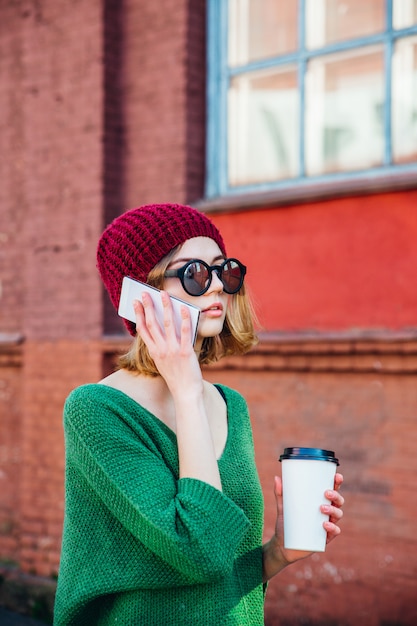 Feliz joven hablando por teléfono móvil y sosteniendo café en la calle de la ciudad