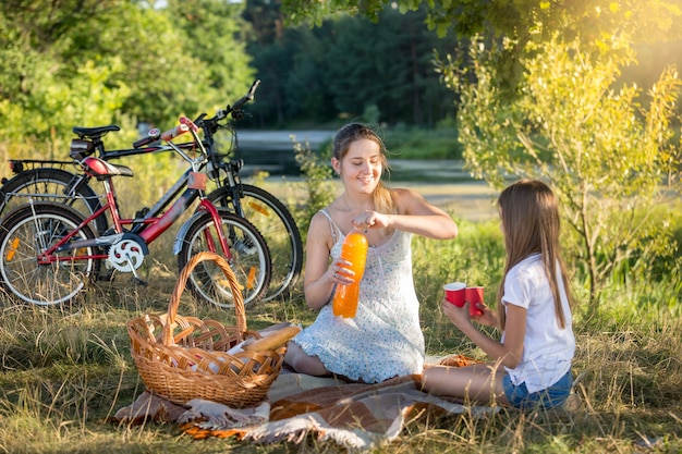 Feliz joven haciendo un picnic junto al río con su hija de 10 años.