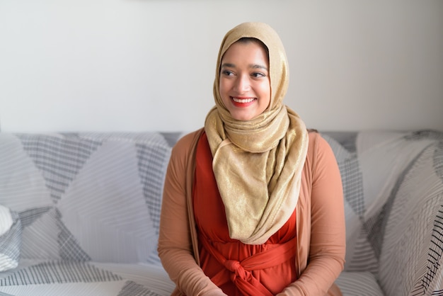Feliz joven hermosa mujer musulmana pensando en la sala de estar en casa