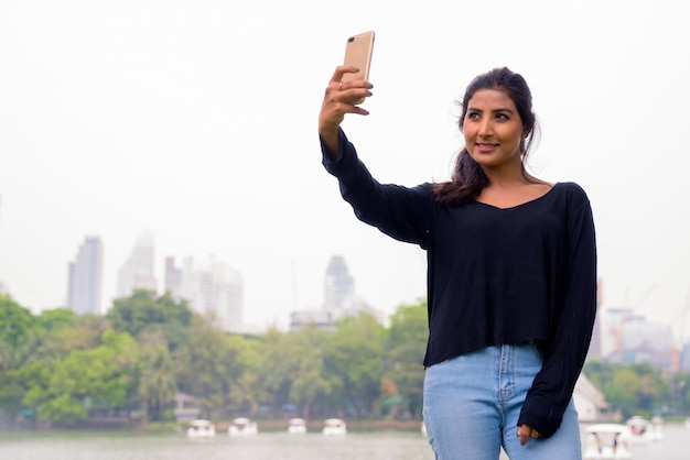 Feliz joven hermosa mujer persa tomando selfie en el parque