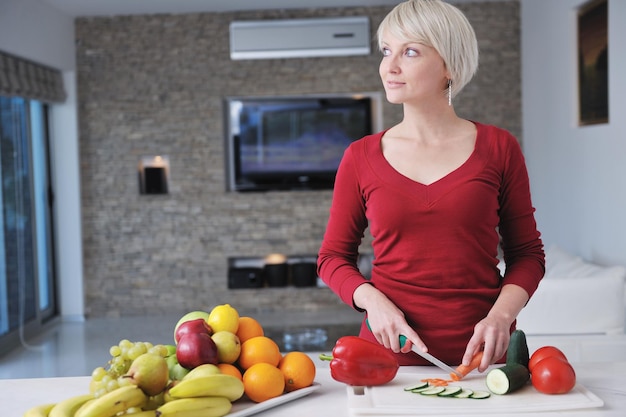 feliz joven hermosa mujer rubia preparar comida en la cocina en casa