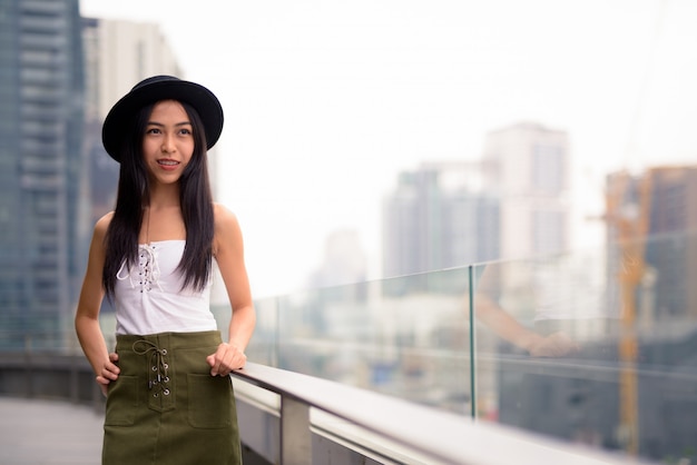Feliz joven hermosa mujer turista asiática pensando en contra de la vista de la ciudad