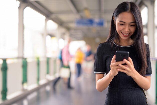 Feliz joven hermosa mujer turista asiática con teléfono en la pasarela