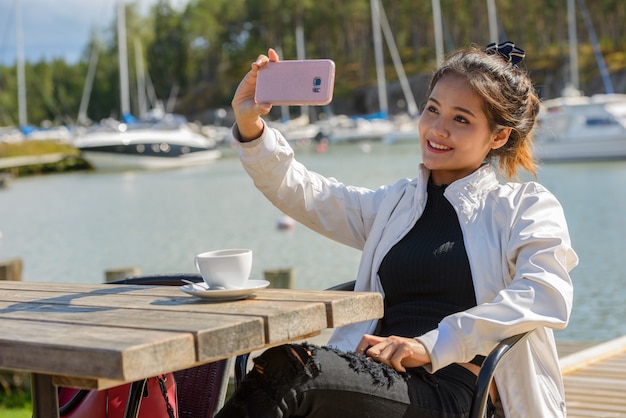 Feliz joven hermosa mujer turista asiática tomando selfie en restaurante junto al muelle
