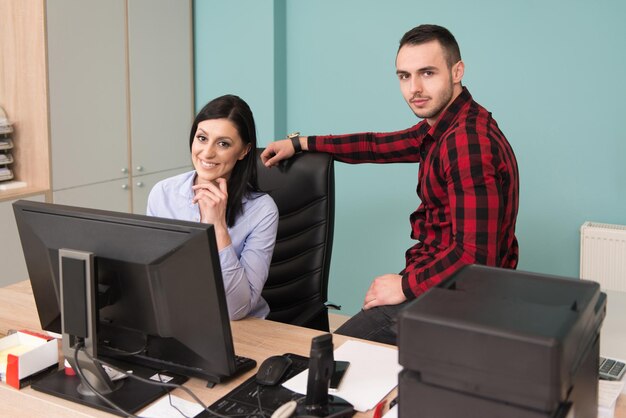 Feliz joven hombre y mujer de negocios trabajan en la oficina moderna en la computadora