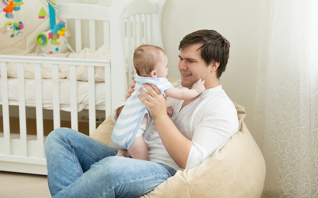 Feliz joven jugando con su bebé en el dormitorio