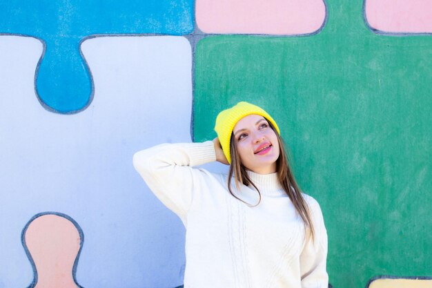 Feliz joven juguetona mantiene las manos en el sombrero vestido con un jersey blanco casual expresa emociones