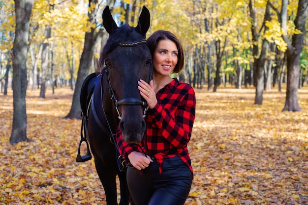 Feliz joven junto al caballo negro en otoño en el parque