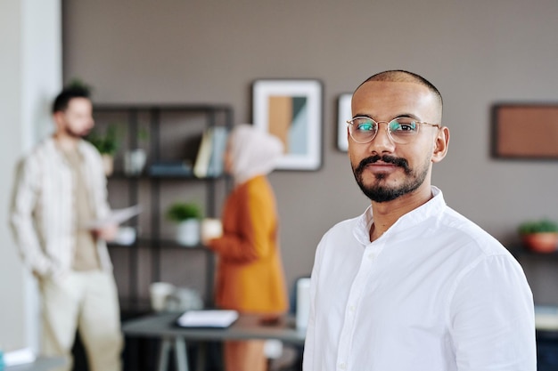 Foto feliz joven líder del equipo de negocios musulmán de pie contra sus compañeros de trabajo