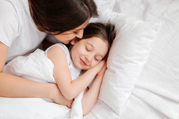 Feliz joven madre abraza a su pequeña hija en la cama