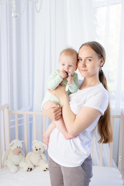 Feliz joven madre con un bebé en brazos en la cuna del dormitorio