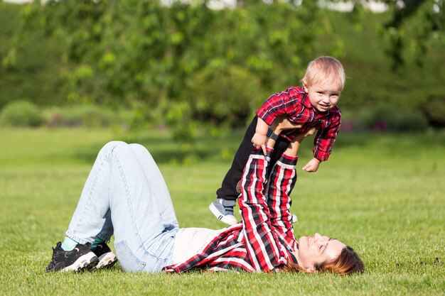 Feliz joven madre está jugando con su bebé en un parque en un césped verde.