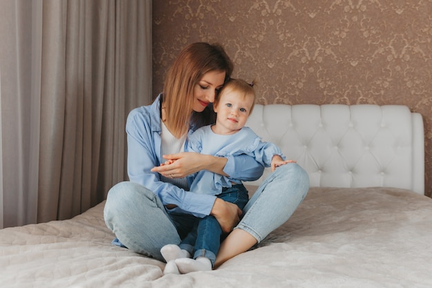 Feliz joven madre juega con su hija en la cama en casa. día de la Madre.